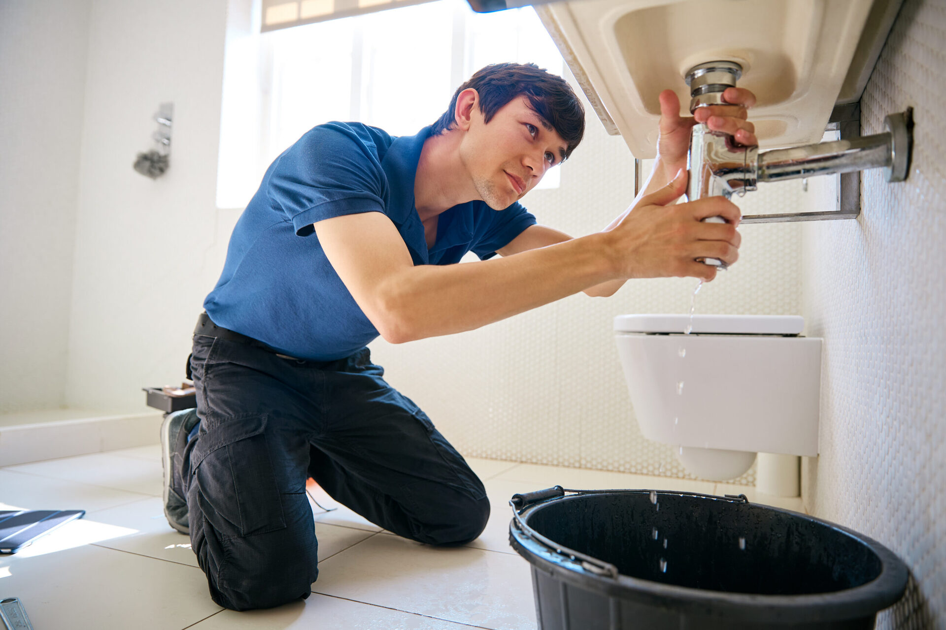 Plumber repairing a water leak under a bathroom sink